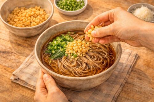 そばに天かすとネギをトッピングしているイラスト